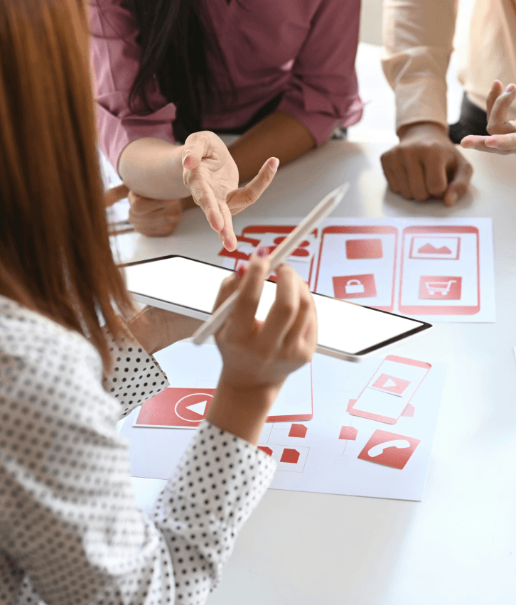 UX strategy and product discovery workshop with designers reviewing wireframes and prototypes on tablet, symbolizing user research, product validation, and experience strategy services.